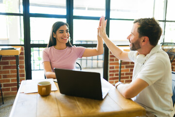 Business partners high-fiving after finishing project in coffee shop
