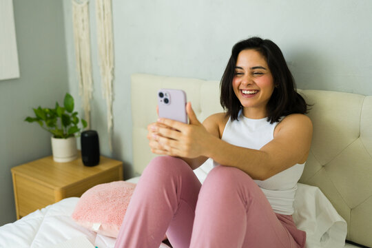 Cute latin woman working from home using smartphone on bed - Powered by Adobe