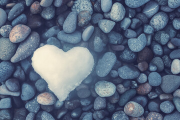 Heart of snow on pebble sea beach in winter, soft focus, top view, romantic background. Holiday...