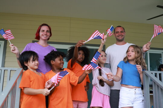 Diverse group of children and two adults teacher celebrating outdoors with waving American flags on USA Independence Day.enjoying a festive patriotic event 