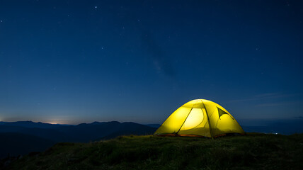 Illuminated camping tent on a grassy hill under a starry night sky stars