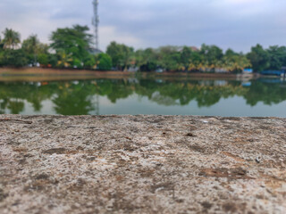 Close up of a rustic concrete surface with a blurred background featuring a tranquil pond...