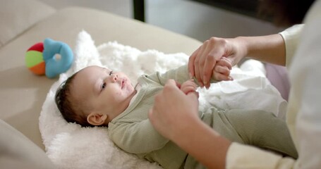 Mother entering from right lifting, lowering infant arms encouraging movement on sofa with ball