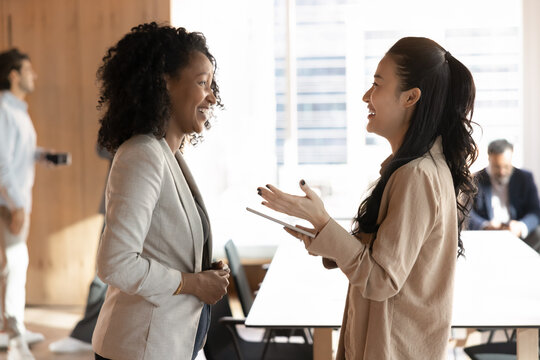 Friendly work atmosphere. Young multiracial businesswomen colleagues laugh talk chat in modern office share professional success celebrate teamwork discuss career achievements in casual conversation