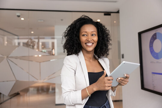 Fototapeta Strategic mindset. Smiling millennial African businesswoman distracted from using digital tablet in modern office look aside planning business goals visualizing ideas reflecting on future achievements