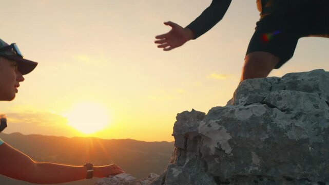 Two runners high-five atop a rocky peak during a stunning sunset, celebrating achievement and camaraderie in cross-country running, captured with an upward angle.