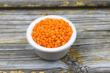 Red lentils in wooden bowl on wooden table background. Top view, copy space. Flat lay.
