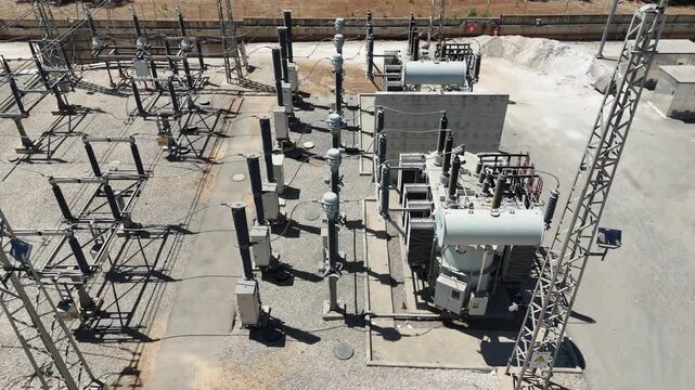 Aerial drone view of an industrial electrical substation with transformers and high-voltage power lines. Infrastructure of the national power grid, captured from above.

