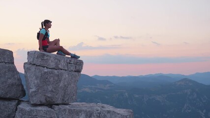 Determined female runner atop rugged mountain peak at dawn, in vibrant athletic gear, symbolizing triumph and connection with nature.