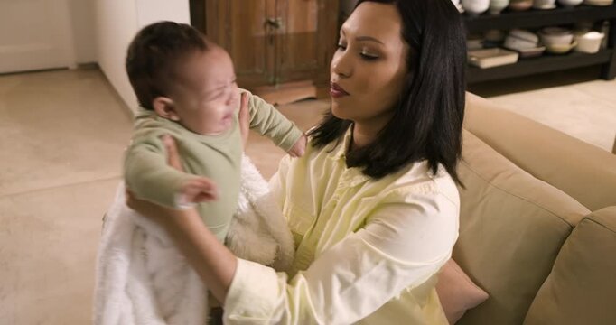 Mother and daughter sitting on sofa draping blanket before baby fussing and cleaning face with wipe