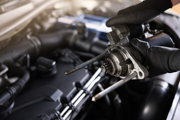Auto part. Professional mechanic with starter motor near open hood of car indoors, closeup
