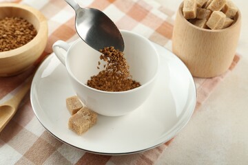 Putting instant coffee into cup at light table, closeup