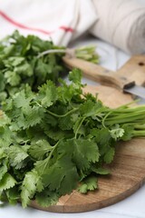 Cutting board with fresh cilantro and knife on white table, closeup