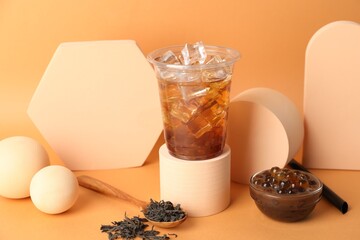 Tasty iced bubble tea and ingredients on orange background