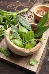 Mortar with different fresh herbs on wooden table, closeup