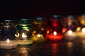 Many grave candles on black table against red background, closeup