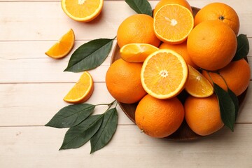 Fresh ripe oranges and leaves on light wooden table, flat lay