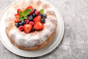 Tasty Bundt cake with powdered sugar and berries on grey textured table, closeup. Space for text
