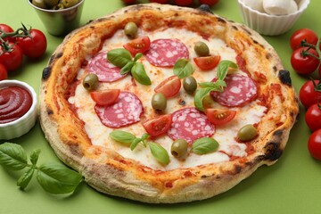 Delicious pizza with salami, olives, tomatoes and basil on green table, closeup