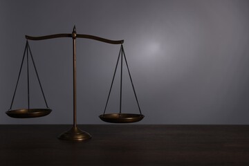 Scales of justice on wooden table against grey background. Space for text