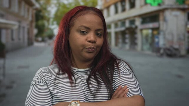 Woman wearing striped shirt with red hair, arms crossed and serious expression in city street; rejection.