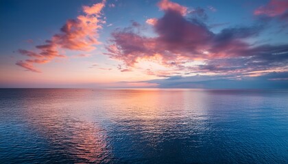 vibrant sunset sky over a calm blue sea with soft pink clouds and golden light reflection creates a peaceful atmosphere