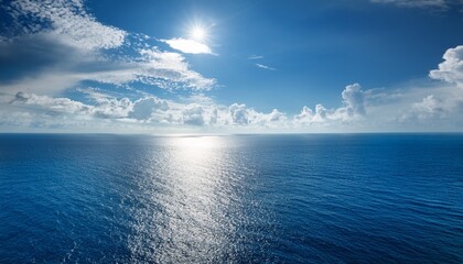 Obraz premium vast ocean under a bright sky with fluffy clouds and sunlight reflection creates a serene atmosphere