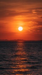 Bright sun setting over dark ocean with orange sky