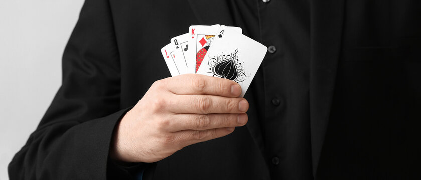 Young man with playing cards for poker on grey background, closeup