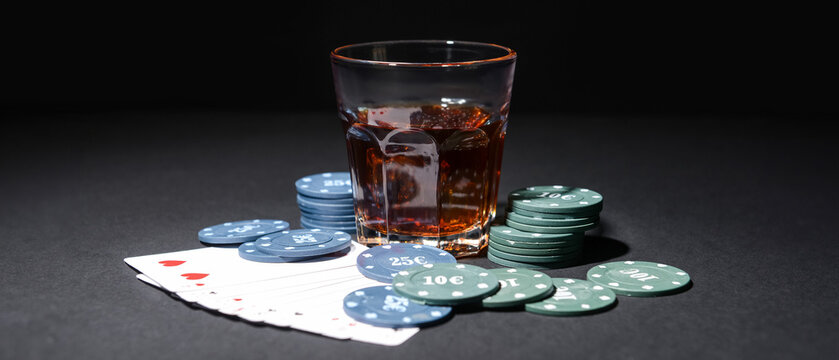 Poker chips, glass of beverage and cards on dark background