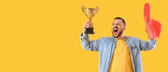 Screaming sport fan with foam hand and golden cup on yellow background