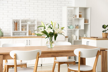 Vase with beautiful lily flowers on wooden dining table in kitchen