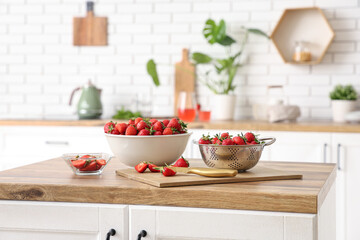 Bowl, colander and board with tasty strawberries on table in kitchen