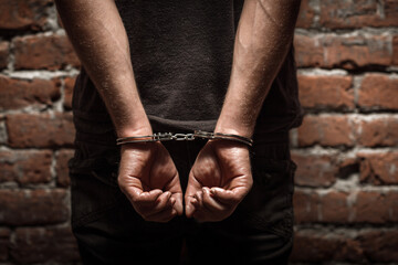 Rear view of a man in handcuffs standing against a brick wall, symbolizing arrest, law enforcement, or criminal justice. Ideal for crime prevention campaigns, legal editorials, or awareness content.

