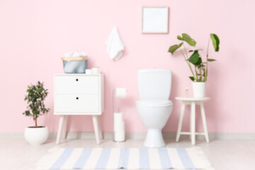 Toilet bowl, bedside table and plants near pink wall in restroom