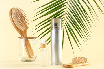 Hair spray with cosmetic serum and brushes on light yellow background