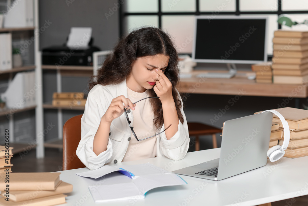 Poster female tired student studying with notebook and laptop at table with stack of books in library