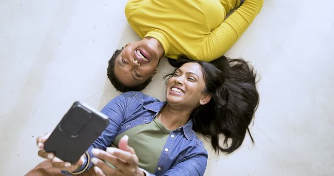 African American and Indian friends lying at home holding smartphone for selfie pouting smiling