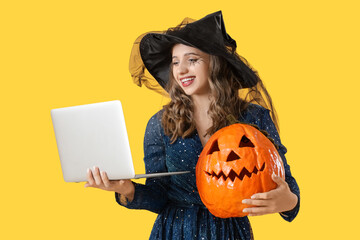 Young woman dressed as witch for Halloween with pumpkin and laptop shopping online on yellow...