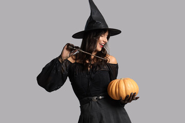 Young witch with wand and pumpkin on light background