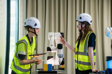 Two women wearing safety gear and holding a tablet. One of them is pointing at the tablet. Team of...