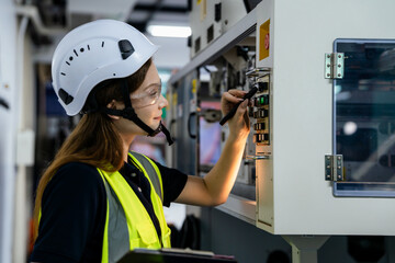A woman in a yellow vest is working on a machine. She is wearing a helmet and goggles. Female...