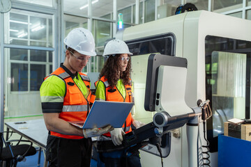 Two people wearing orange vests and hard hats are working on a computer. Team of diverse engineers,...