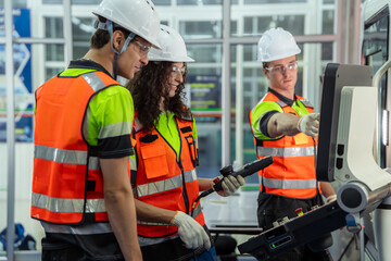 Three people wearing orange vests. Group of machinists in an on-the-job training session, learning...