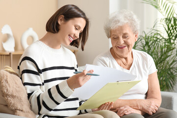 Smiling nurse with clipboard and senior woman sitting on sofa at home