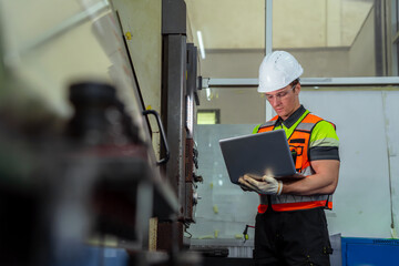 A man wearing a safety vest and a hard hat is looking at a laptop. Professional engineer engaged in...