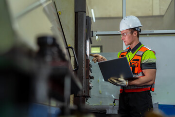 A man wearing a safety vest and a hard hat is looking at a laptop. Professional engineer engaged in...