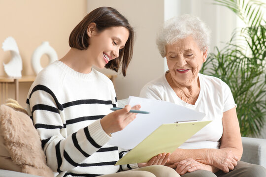 Smiling nurse with clipboard and senior woman sitting on sofa at home - Powered by Adobe