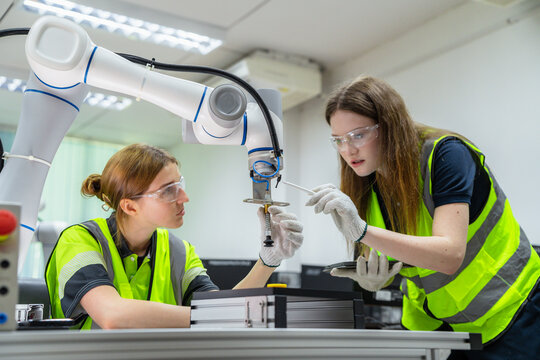 Two women wearing safety gear are working on a robot. Female students in a university robotics class learning to program a collaborative robot (cobot).