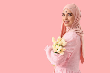 Beautiful Muslim woman in hijab with tulips on pink background